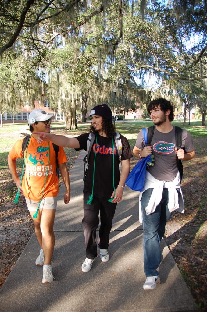 Male students walking across UF campus on sidewalk, pointing as they reflect on sustainability goals.