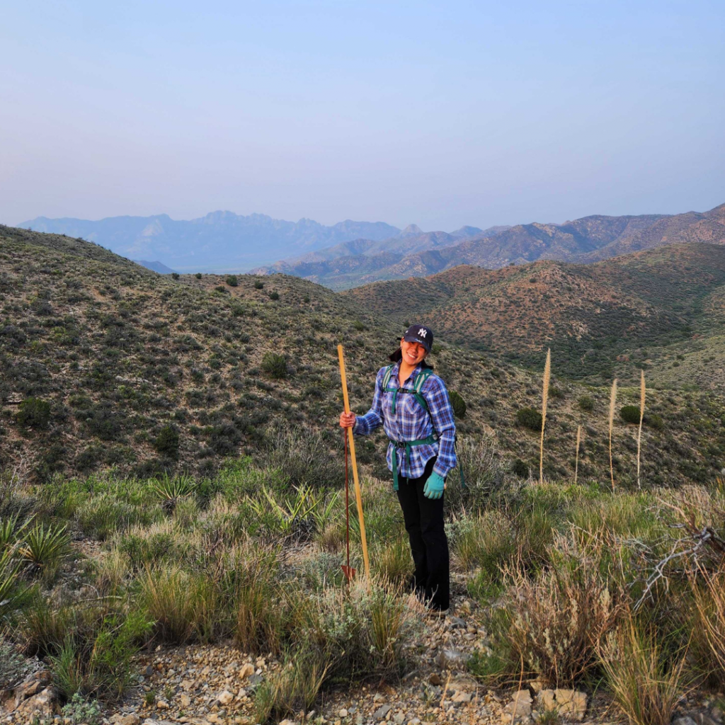 UF Biodiversity Intern Emily Martucci stands in a field surrounded by mountains.