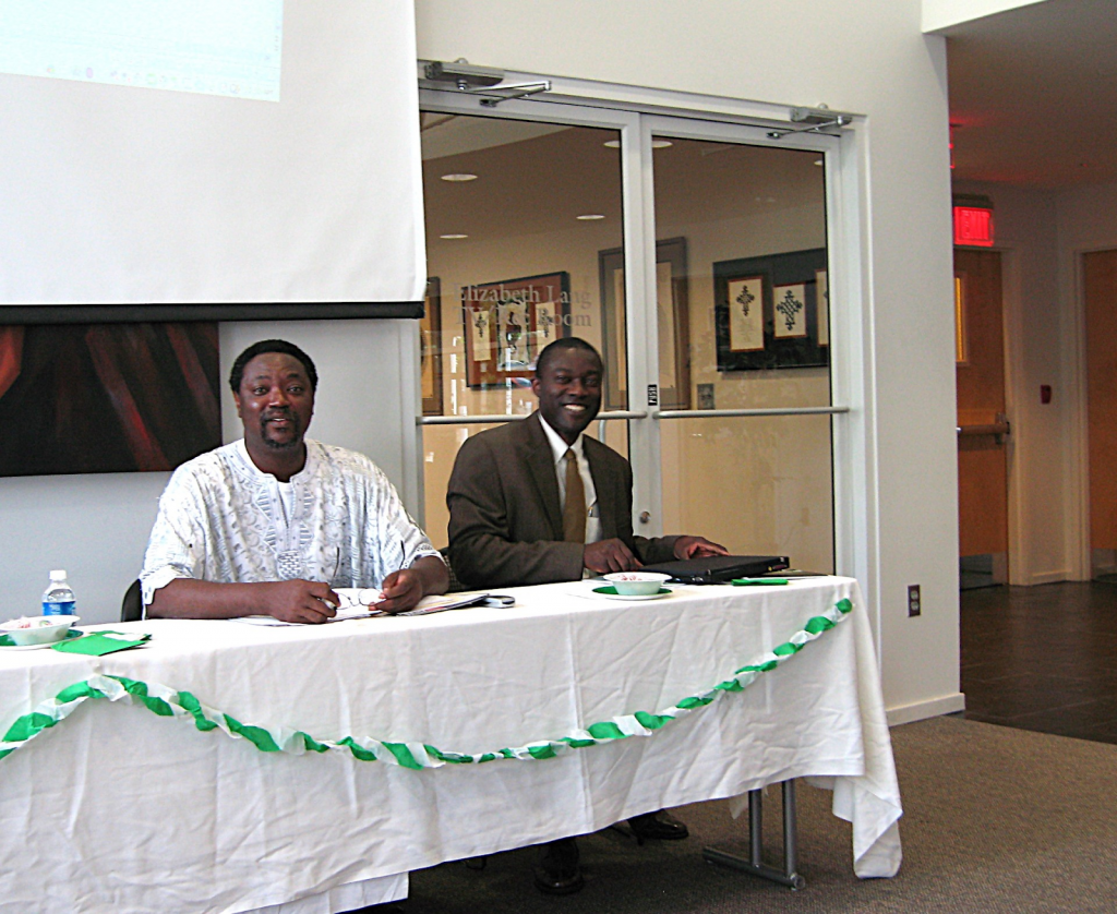 Dr. Kole Ade-Odutola and colleague sit at a table on campus.