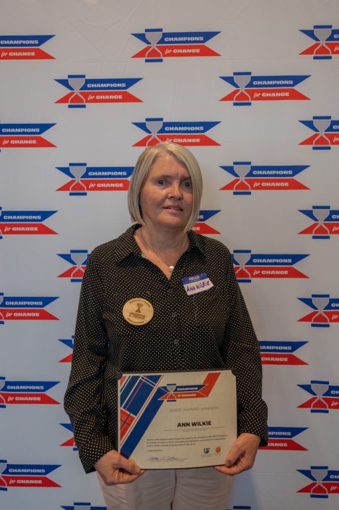 2025 Champions for Change Award Recipient, Ann Wilkie, pose with their award certificate.
