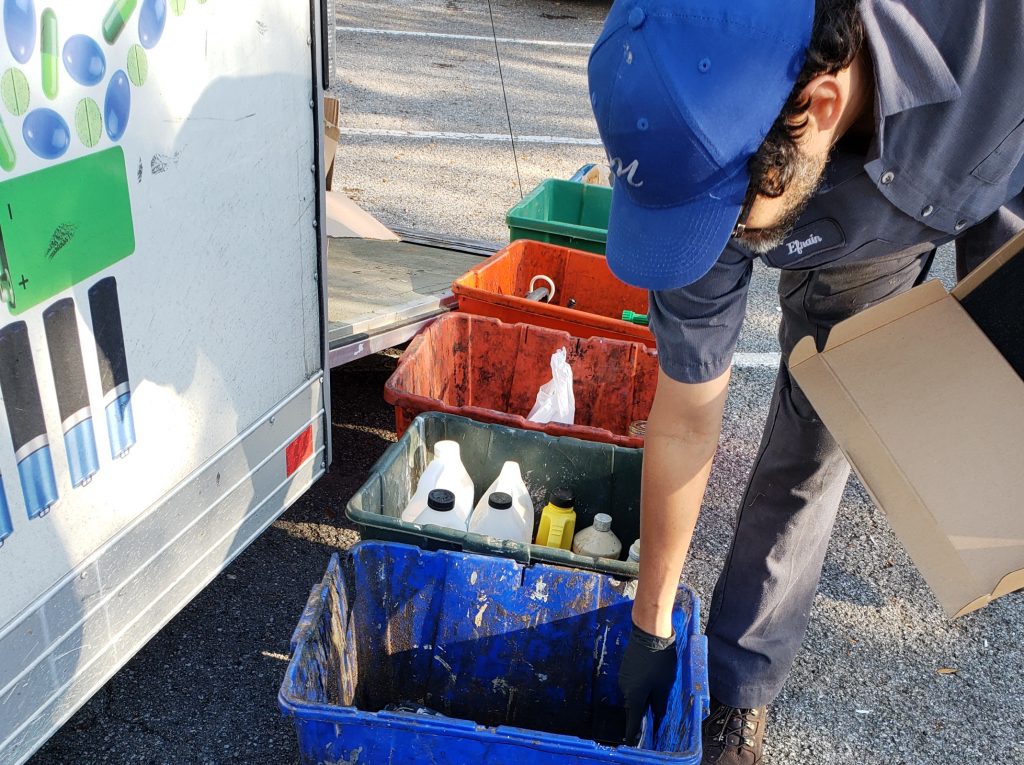 Man places material into blue recycling bin. Green and orange bins are visible behind him.