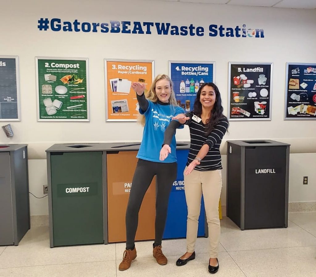 Two student volunteers doing the Gator Chomp infront of the GatorsBeatWaste Station