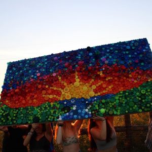 Mayssa holding up the bottle cap mural made by the student organization UNLITTER. 